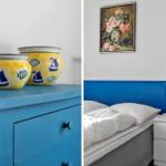 Bedroom with blue headboard, white bedside lamp, and painting on the wall.