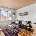 Living room with sofa, two leather chairs, and glass table. Wooden ceiling and window with view.