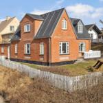 Red brick house with white windows and fence. Garden with sun lounger.