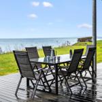 Deck with table and chairs, view of sea and grassy area.