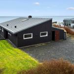 Modern villa with sea view and terrace. Black facade, green lawn, and gravel path.