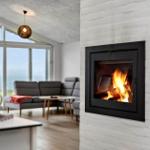 Fireplace with burning fire in white wall. Background shows living room with sofa and window.