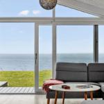 Living room with sea and grass view. Sofa, table, and windows visible.