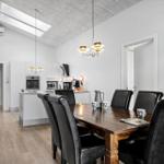 Dining area with wooden table and black leather chairs. Kitchen with white cabinets and range hood.