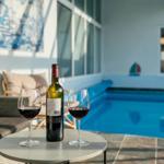 Round table with wine glasses and bottle in front of pool and lounge area