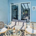 Terrace with rattan furniture, glass table, and bottle. Background: blue wall and glass door.