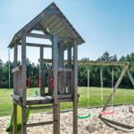 Wooden playground with slide, swings, and sandbox on green lawn.