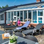 Terrace with sun loungers and view into the glass conservatory with pool.