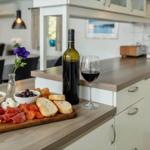 Kitchen with wooden board, wine, cheese, sausage, and fruit.