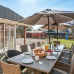 Terrace with table, chairs, and umbrella. Playground and garden in the background.