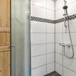 Shower cabin with glass door and showerhead, wall tiles with mosaic strip.