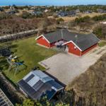 Red vacation house with garden, playground, and barbecue area. View of coastal landscape.