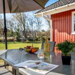Terrace with table, chairs, and umbrella. Background: garden with trampoline and house wall.
