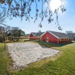 Red vacation house with sand volleyball court on green lawn.