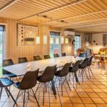 Dining area with long table and chairs, living area with leather sofas and windows.