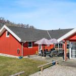 Red vacation house with terrace, table, chairs, and umbrellas. Lawn and trees in the background.