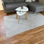 Ein grauer Ecksofa mit Kissen und zwei weißen Tischen auf Teppich.