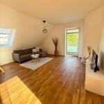 Wohnzimmer mit Sofa, TV und Balkontür. Holzboden und Dachschräge.