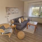 Wohnzimmer mit Sofa, Sessel und Holztisch. Fenster mit Blick auf Garten.