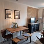 Essbereich mit Holztisch, Stühlen und TV-Schrank an der Wand.