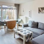 Wohnzimmer mit Sofa, Tisch und Sitzgelegenheiten. Durchgang zum Garten mit Tisch und Stühlen.