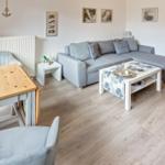 Wohn- und Essbereich mit grauem Sofa, Holztisch und hellen Wänden.