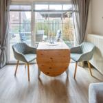 Esszimmer mit Tisch und zwei Stühlen, Blick auf Garten durch Glasfront.