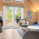 Wohnzimmer mit Kamin, Sofa und Sessel. Durchgang zur Terrasse mit Blick auf Wald.