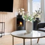 Wohnzimmer mit Kamin, Glas-Tisch und Sessel. Holzwand und großes Fenster.