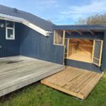 Ein Holzveranda mit offener Garage und Terrasse an einem Haus mit dunkelblauer Fassade.