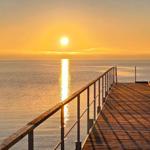 Holzsteg führt zum Horizont, Sonne spiegelt sich im Wasser.