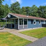 Ein graues Ferienhaus mit Terrasse, Liegestühlen und Grünfläche. Hinterhof mit Zaun.