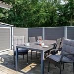 Terrasse mit Tisch und Stühlen, umgeben von grauen Wänden und Bäumen.