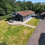 Ein Ferienhaus mit Terrasse, Grillplatz und Rasenfläche. Umgeben von Bäumen und einem Kiesweg.