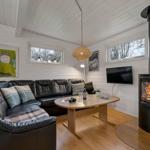 Wohnzimmer mit schwarzer Ledercouch, Kamin und Holztisch. An den Wänden hängen Bilder.