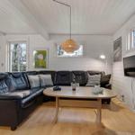 Wohnzimmer mit schwarzer Ledercouch, Holztisch und Kaminofen. Weiße Wände und Holzboden.