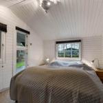 Schlafzimmer mit Bett, Fenstern und Wandbild. Decke mit Holzverkleidung.