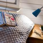 Ein Bett mit einer Decke, einem Buch und einer Lampe neben einem Nachttisch.