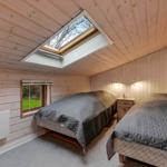 Zwei Betten in einem Zimmer mit Holzwand und Dachfenster. Kleines Fenster und Nachttisch.