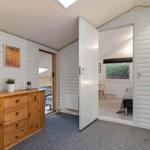 Wohnraum mit Holzschrank und Blick in Schlafzimmer mit Bett und Fenster.