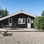 Schwarzes Holzhaus mit weißem Dach, Terrasse und Garten. Gartenmöbel und Spielzeugkiste sichtbar.