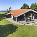 Schwarzes Haus mit Terrasse und Garten. Blick auf das Meer. Holztisch mit Stühlen.