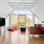 Living room with wooden floor, sofa, TV, and large window with view of nature.
