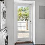 Washing machine and dryer next to a door with view of a paved outdoor area.