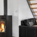 Black wood-burning stove, black leather sofa with green cushions, wooden staircase.