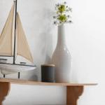 A model boat and a vase with flowers are on a wooden shelf.