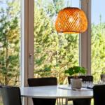 Dining area with table, chairs, and pendant lamp. View of green trees through large windows.