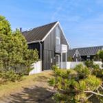 Black wooden house with balcony and skylight, surrounded by pine trees and white fence.