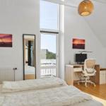 Bedroom with double bed, desk, and TV. Large windows and wooden floor.