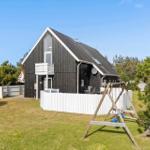 Black wooden house with white fence and swing in the garden.